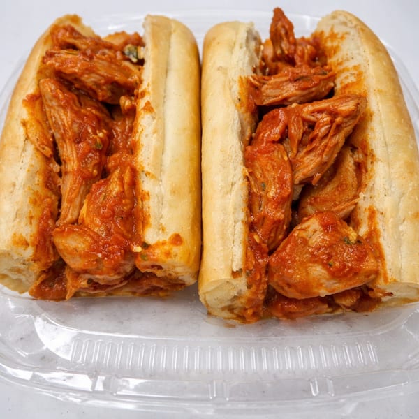 Two chicken parmesan subs with red sauce in a clear plastic container on a white surface.