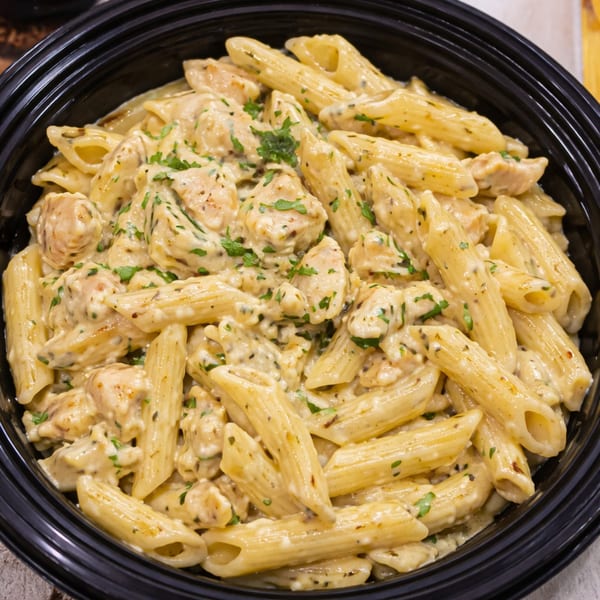 Creamy penne pasta with chicken and herbs in a black bowl.