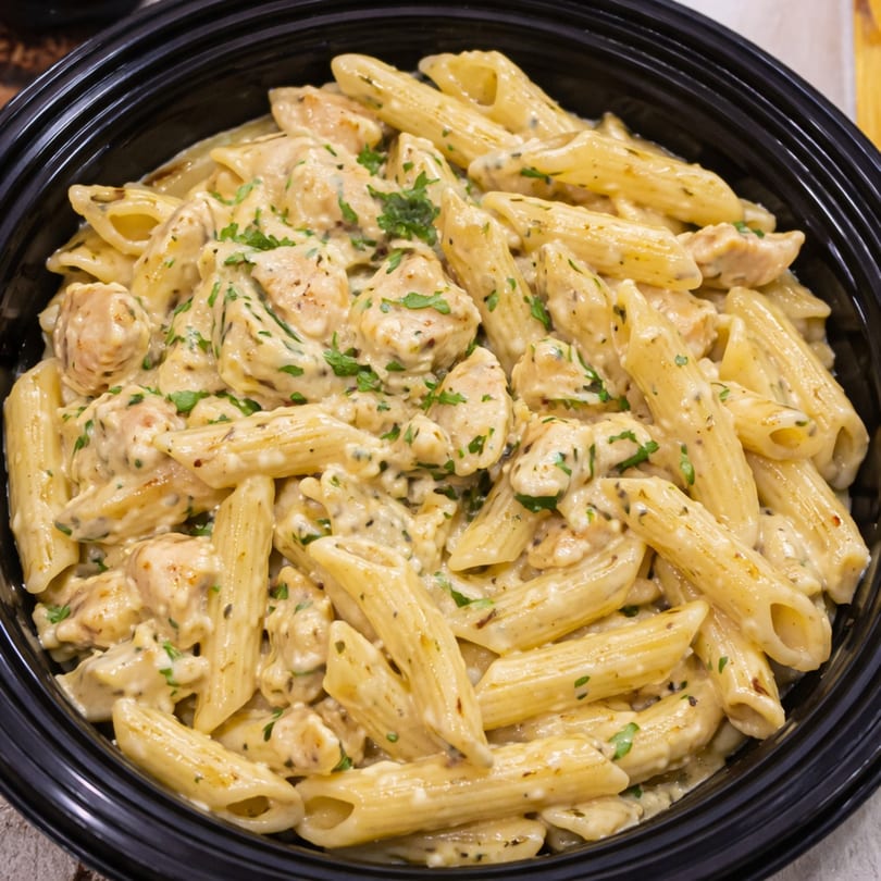 Creamy penne pasta with chicken and herbs in a black bowl.