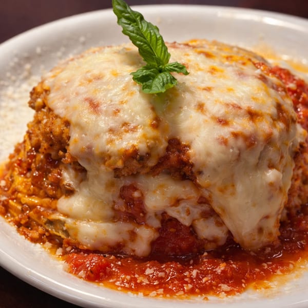 A close-up of a cheesy lasagna with rich red sauce and a fresh basil garnish.